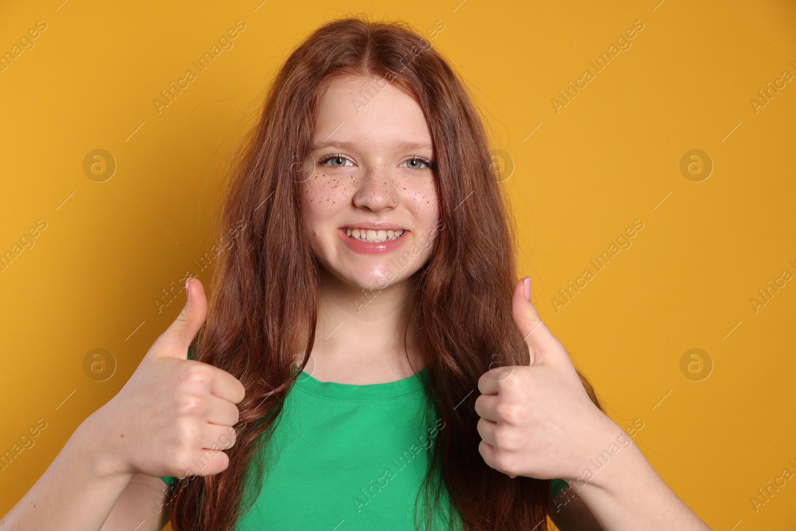 Photo of Beautiful teenage girl with freckles showing thumbs up on orange background