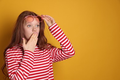 Photo of Surprised freckled teenage girl with sunglasses on orange background, space for text