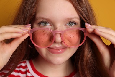 Beautiful freckled teenage girl with sunglasses on orange background, closeup