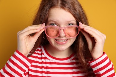 Beautiful freckled teenage girl with sunglasses on orange background