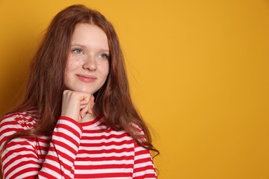 Beautiful teenage girl with freckles on orange background, space for text