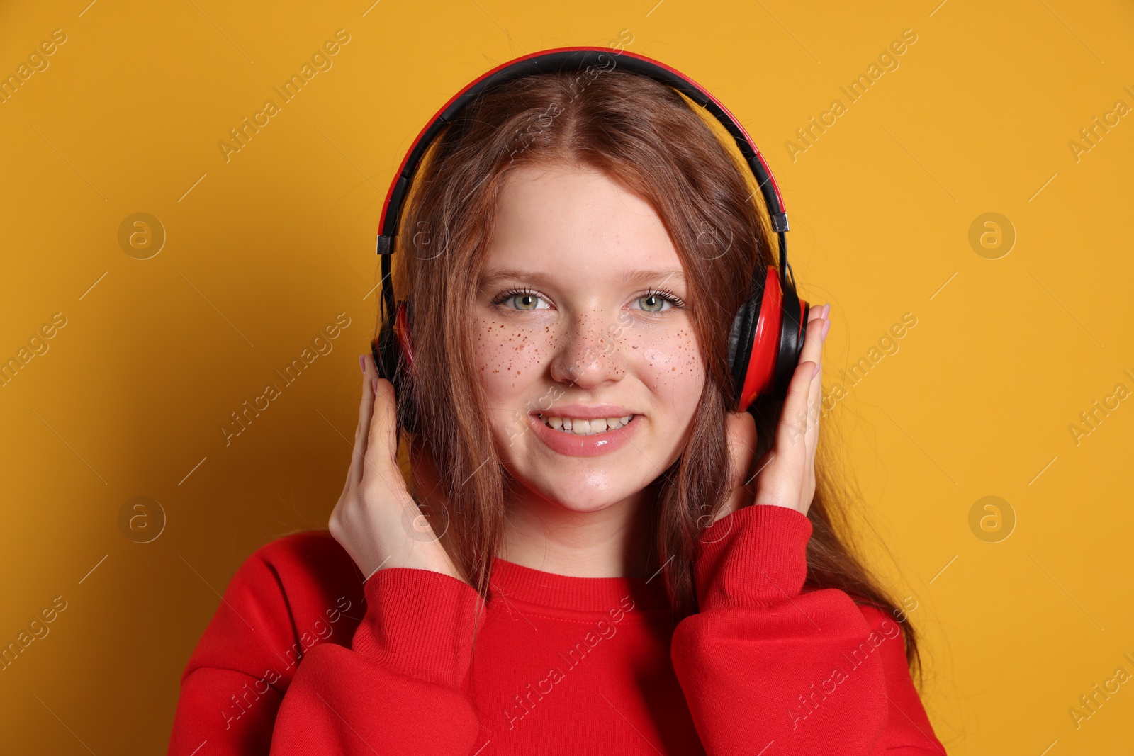 Photo of Beautiful freckled teenage girl with headphones on orange background