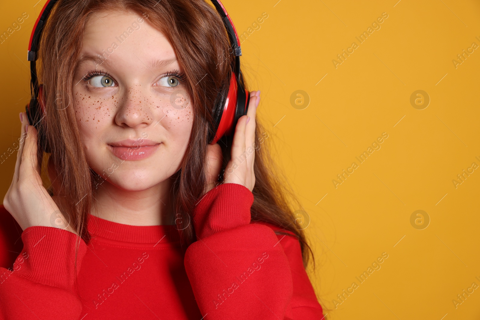 Photo of Beautiful freckled teenage girl with headphones on orange background, space for text