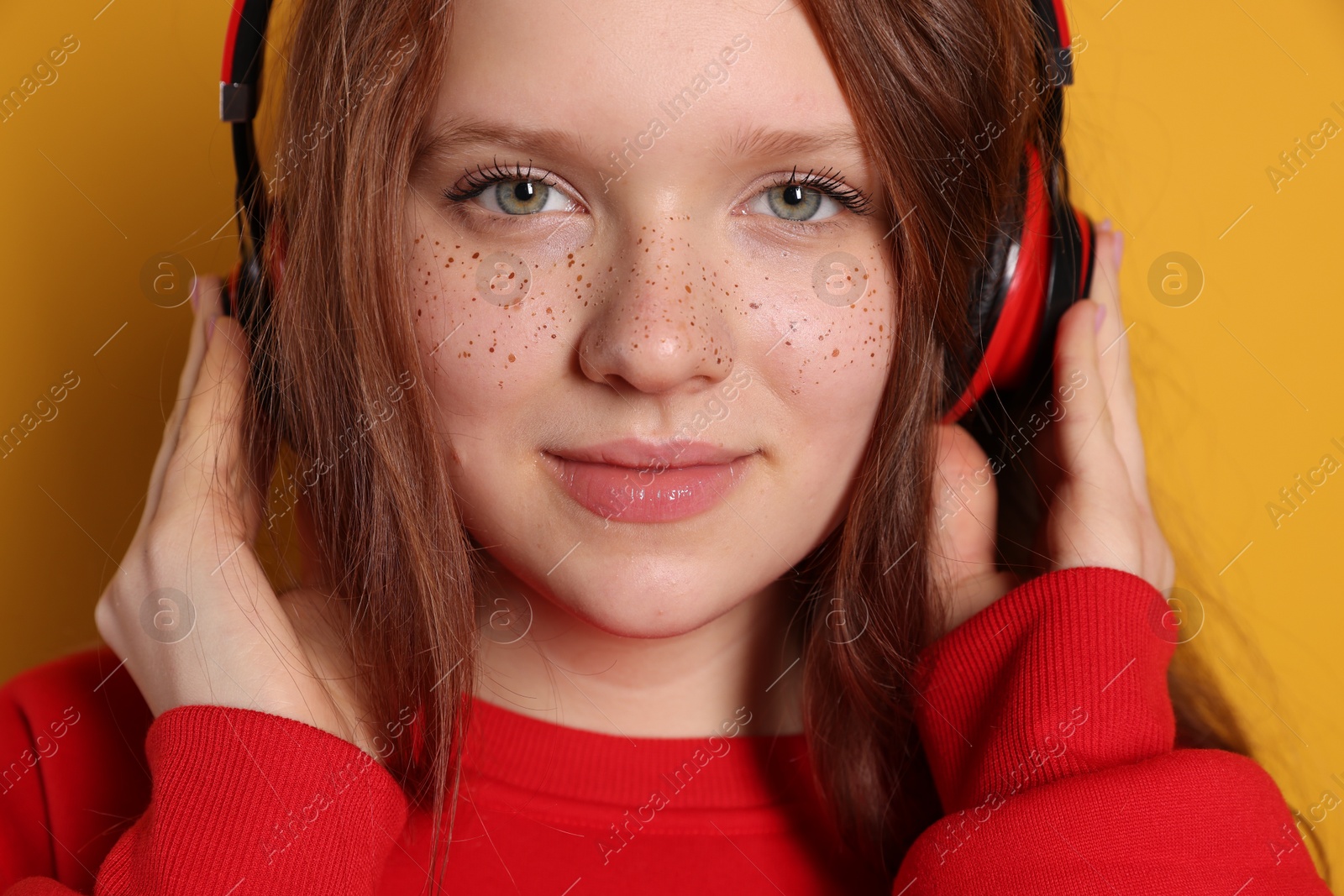 Photo of Beautiful freckled teenage girl with headphones on orange background, closeup