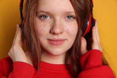 Beautiful freckled teenage girl with headphones on orange background, closeup