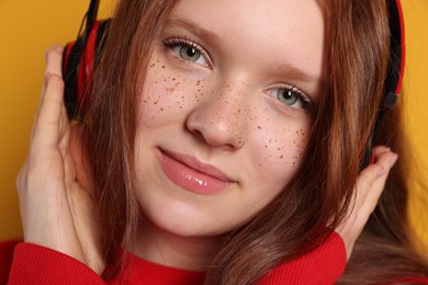 Beautiful freckled teenage girl with headphones on orange background, closeup