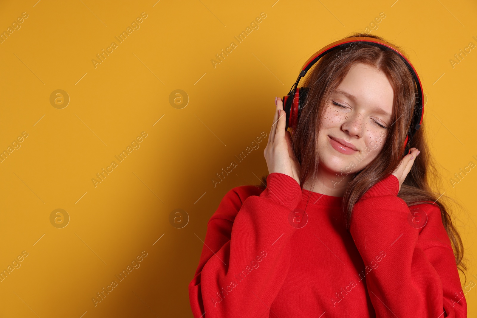 Photo of Beautiful freckled teenage girl with headphones on orange background, space for text