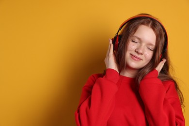 Photo of Beautiful freckled teenage girl with headphones on orange background, space for text