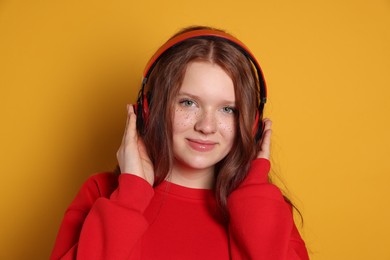 Beautiful freckled teenage girl with headphones on orange background