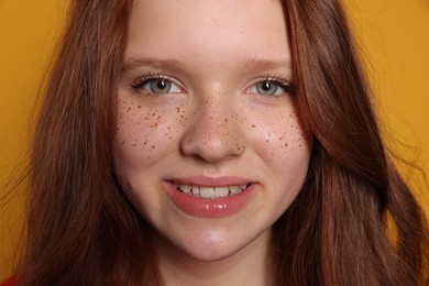 Beautiful teenage girl with freckles on orange background, closeup