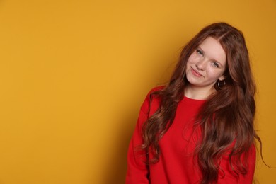 Beautiful teenage girl with freckles on orange background, space for text