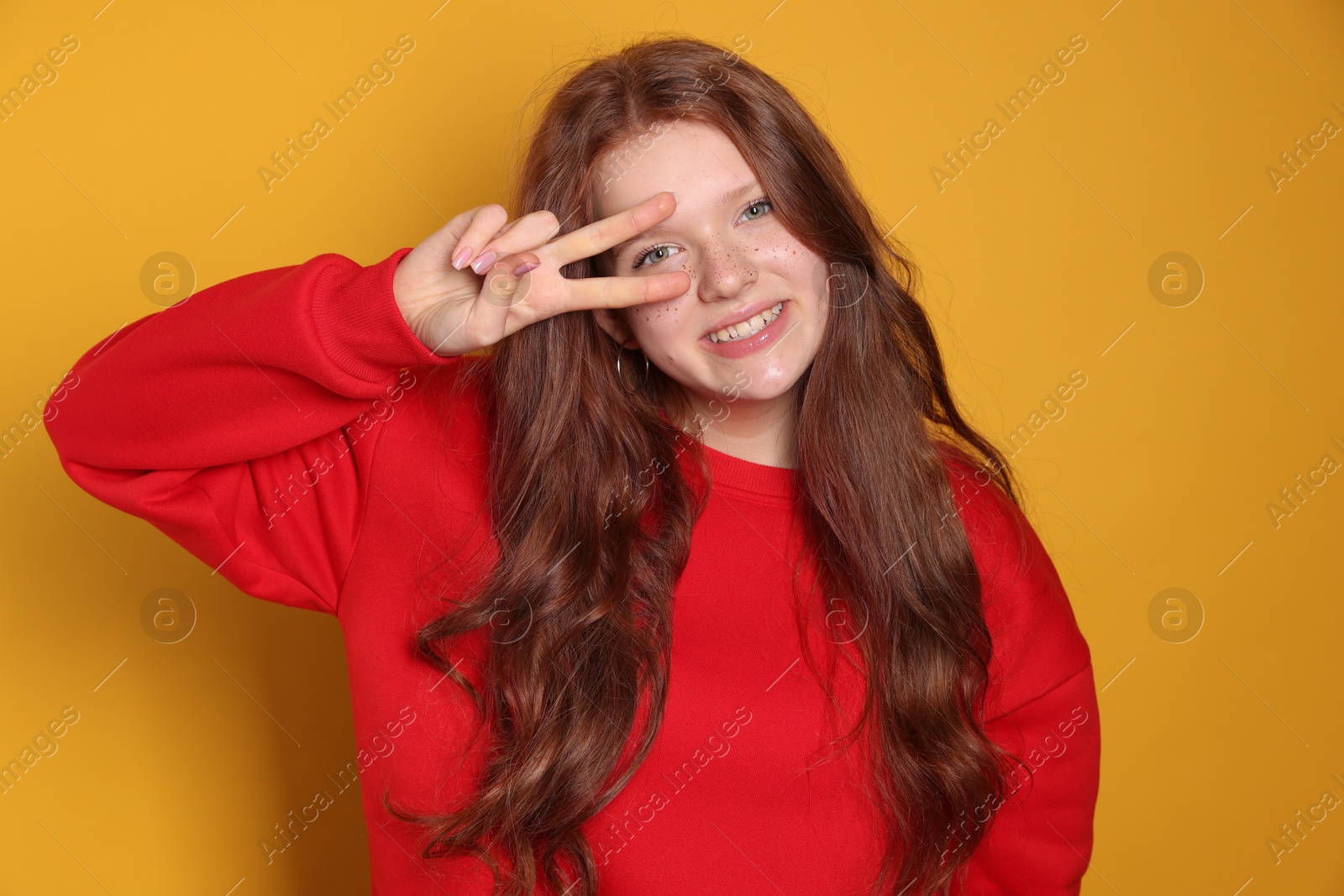 Photo of Beautiful teenage girl with freckles showing V-sign on orange background