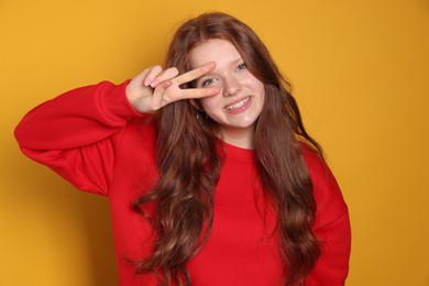 Beautiful teenage girl with freckles showing V-sign on orange background