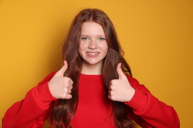 Photo of Beautiful teenage girl with freckles showing thumbs up on orange background