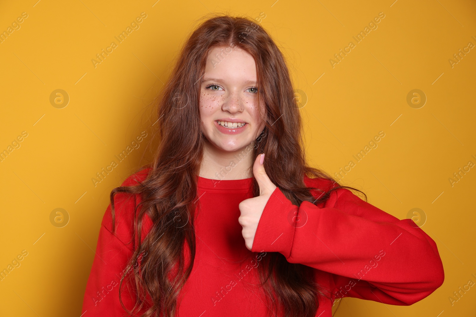 Photo of Beautiful teenage girl with freckles showing thumbs up on orange background