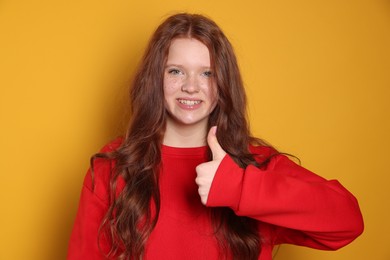 Photo of Beautiful teenage girl with freckles showing thumbs up on orange background