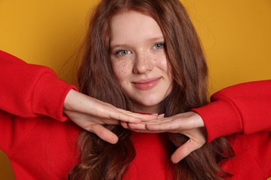 Beautiful teenage girl with freckles on orange background, closeup