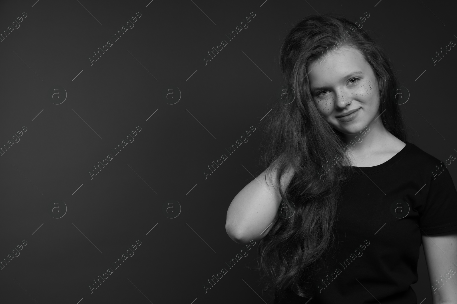 Photo of Beautiful teenage girl with freckles on dark background, space for text. Black and white effect