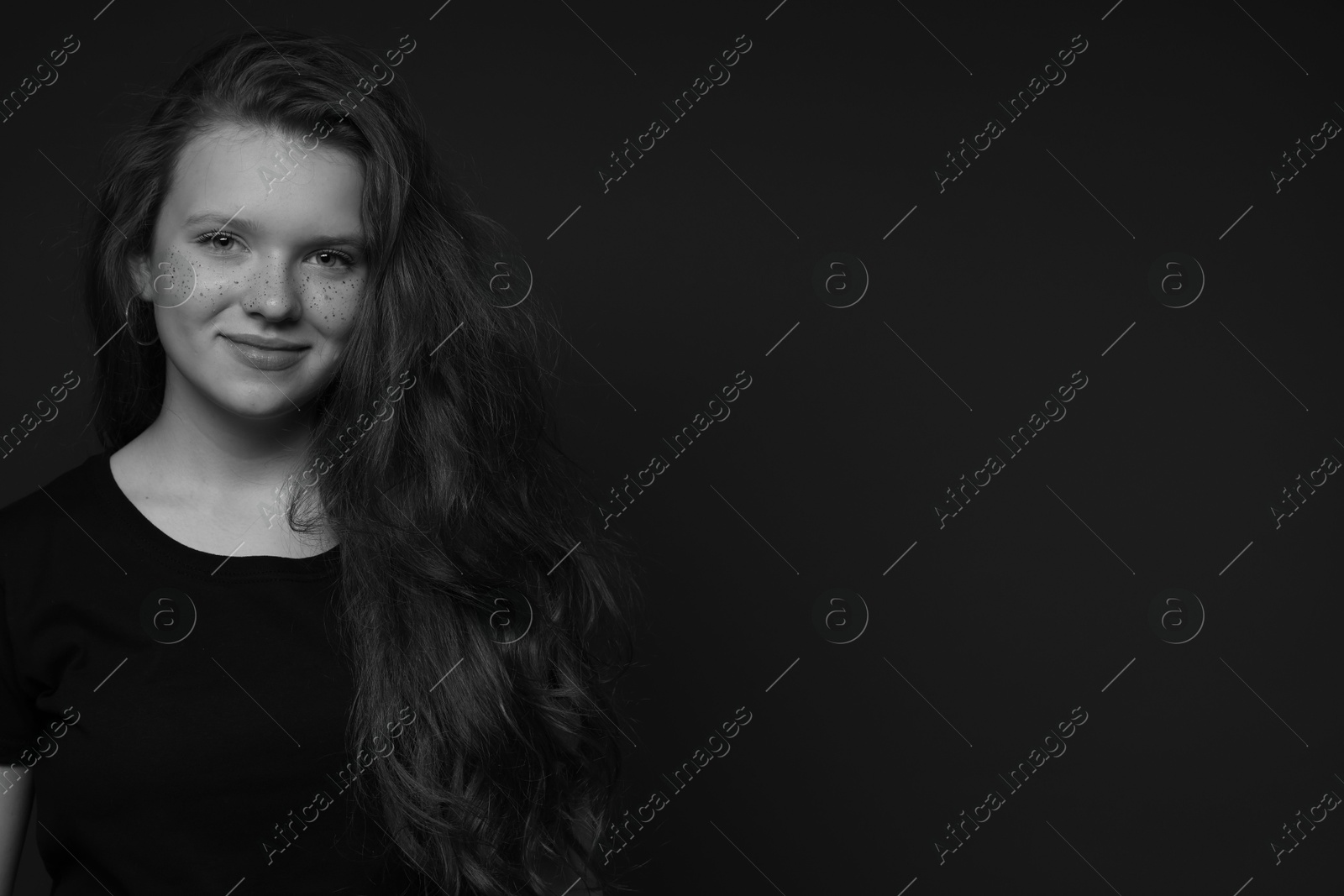 Photo of Beautiful teenage girl with freckles on dark background, space for text. Black and white effect