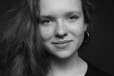 Photo of Beautiful teenage girl with freckles on dark background, closeup. Black and white effect