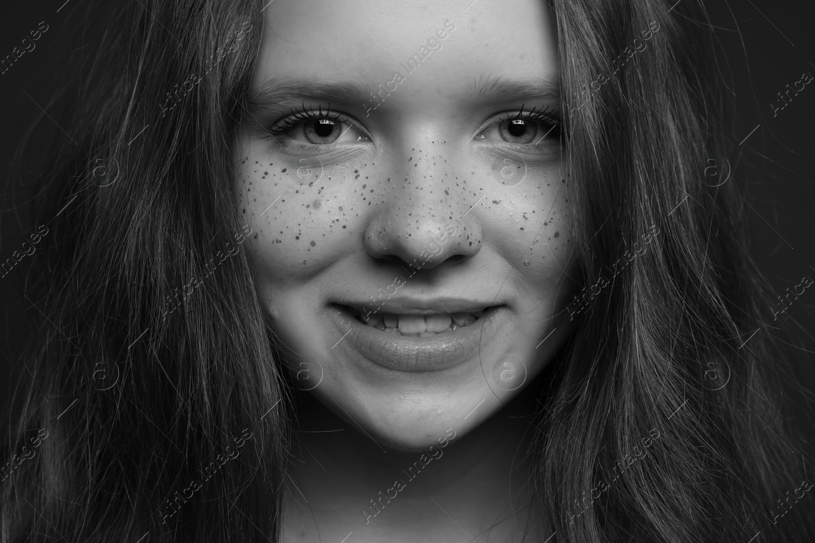 Photo of Beautiful teenage girl with freckles on dark background, closeup. Black and white effect