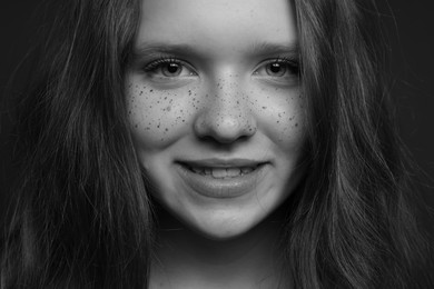 Photo of Beautiful teenage girl with freckles on dark background, closeup. Black and white effect