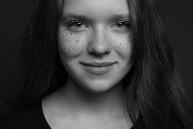 Beautiful teenage girl with freckles on dark background, closeup. Black and white effect