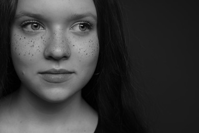 Beautiful teenage girl with freckles on dark background, closeup. Black and white effect