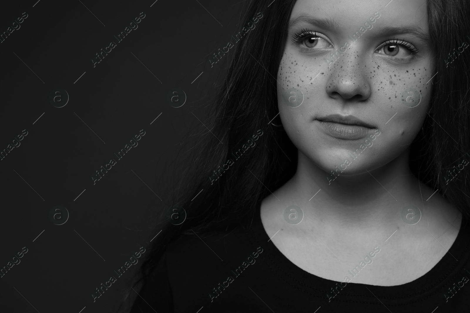 Photo of Beautiful teenage girl with freckles on dark background, closeup and space for text. Black and white effect