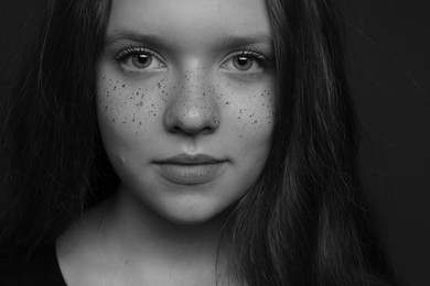 Photo of Beautiful teenage girl with freckles on dark background, closeup. Black and white effect