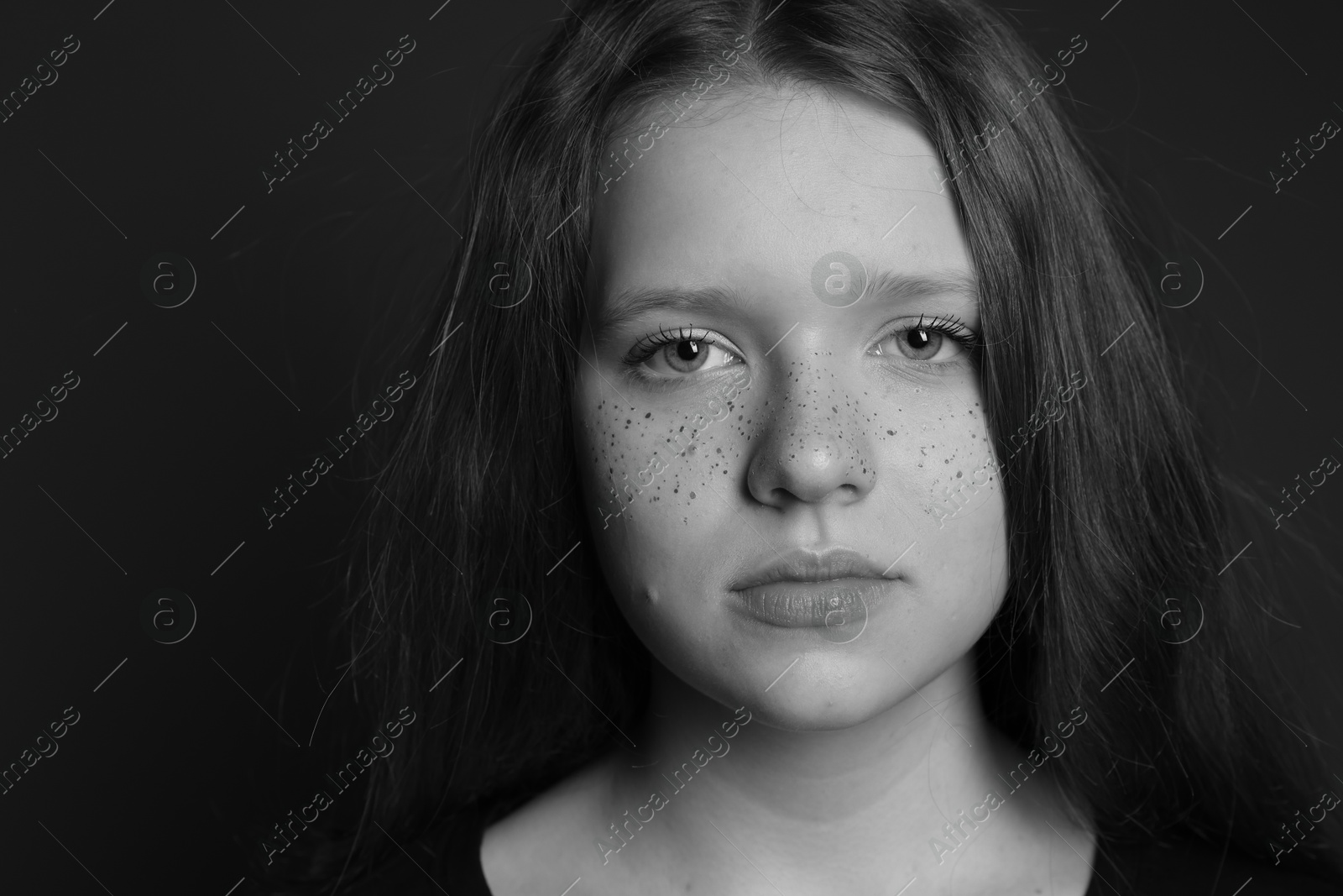 Photo of Beautiful teenage girl with freckles on dark background, closeup. Black and white effect