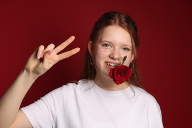 Beautiful freckled teenage girl with rose showing V-sign on red background