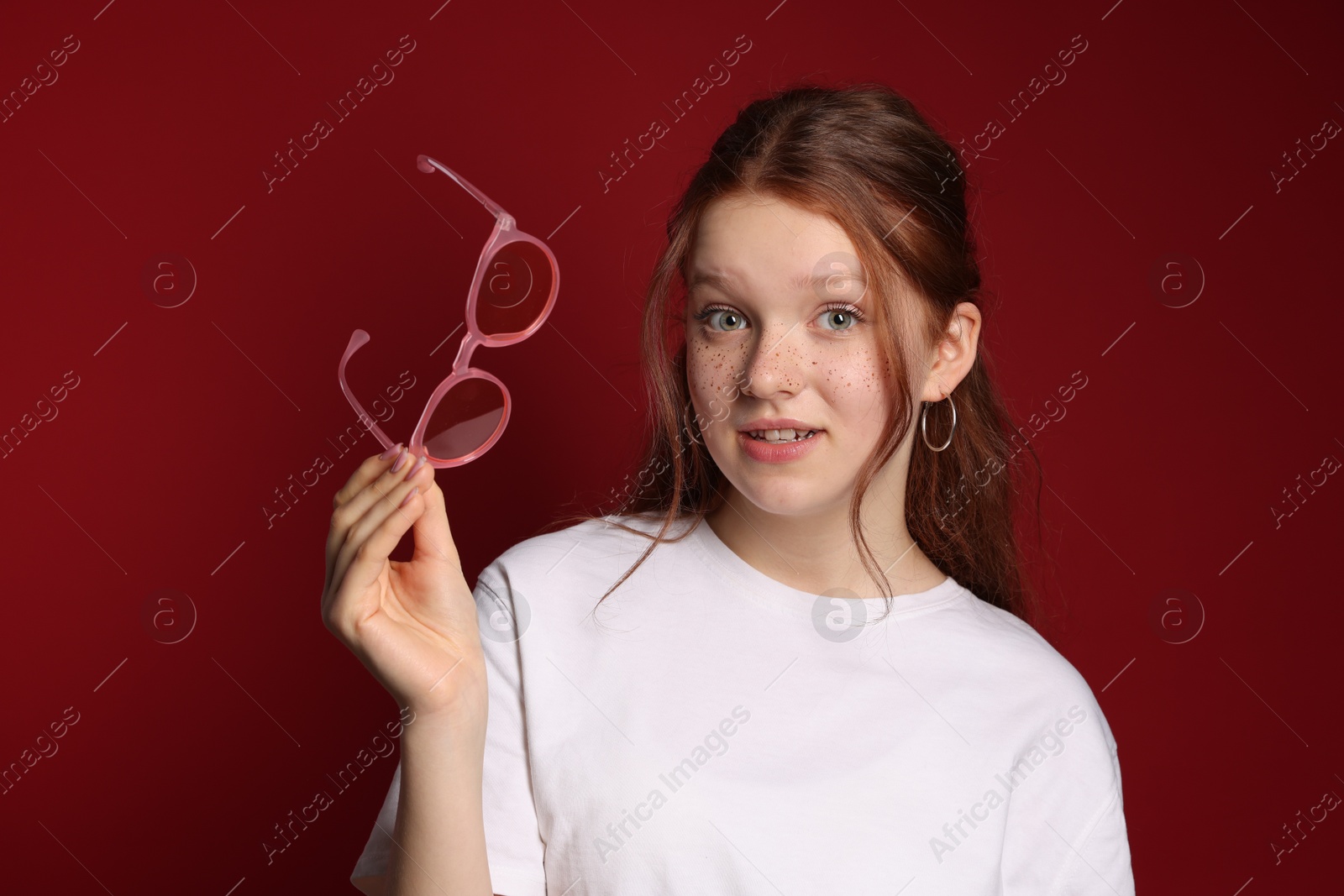 Photo of Beautiful freckled teenage girl with sunglasses on red background