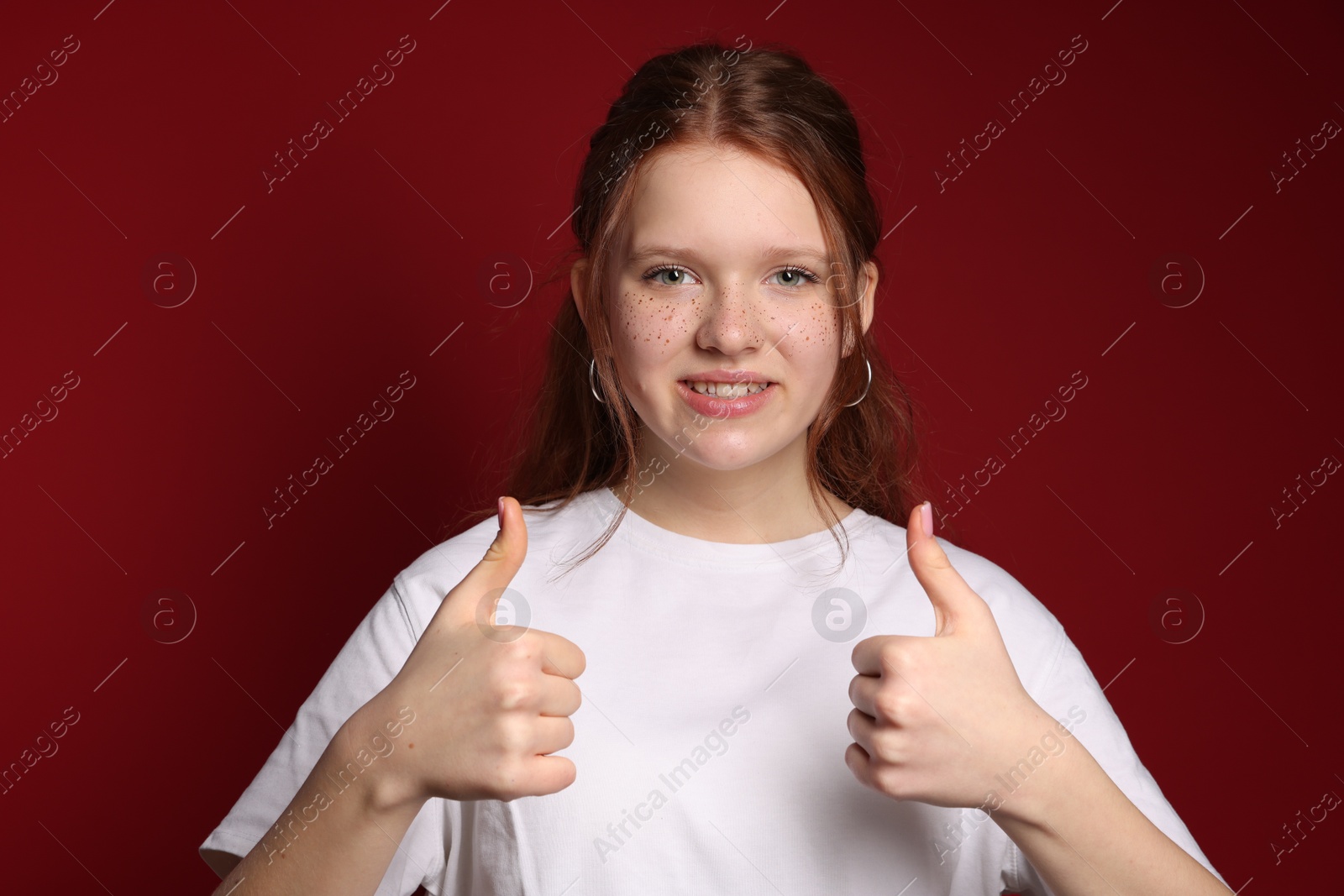 Photo of Beautiful teenage girl with freckles showing thumbs up on red background