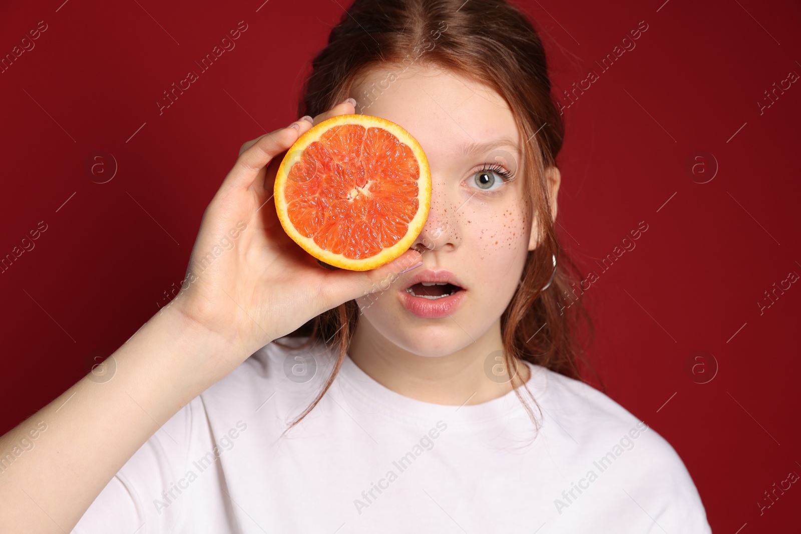 Photo of Beautiful teenage girl with freckles holding grapefruit slice on red background