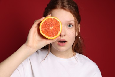 Photo of Beautiful teenage girl with freckles holding grapefruit slice on red background