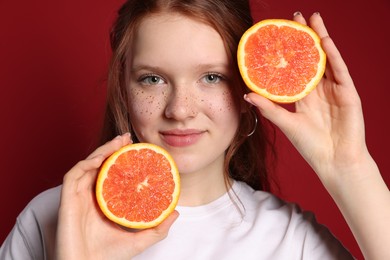 Photo of Beautiful teenage girl with freckles holding grapefruit slices on red background