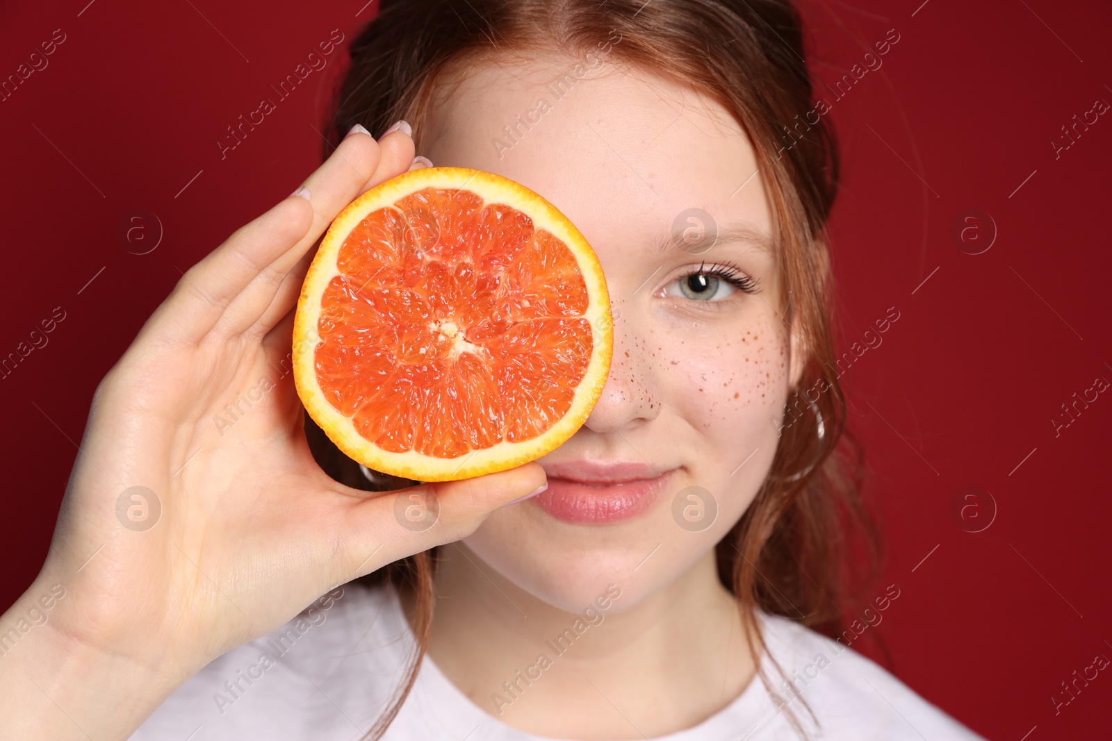 Photo of Beautiful teenage girl with freckles holding grapefruit slice on red background, closeup