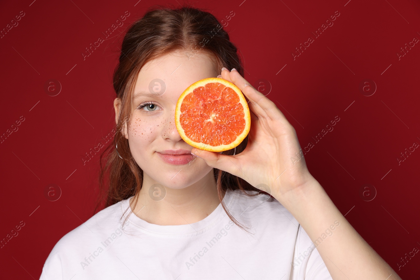 Photo of Beautiful teenage girl with freckles holding grapefruit slice on red background