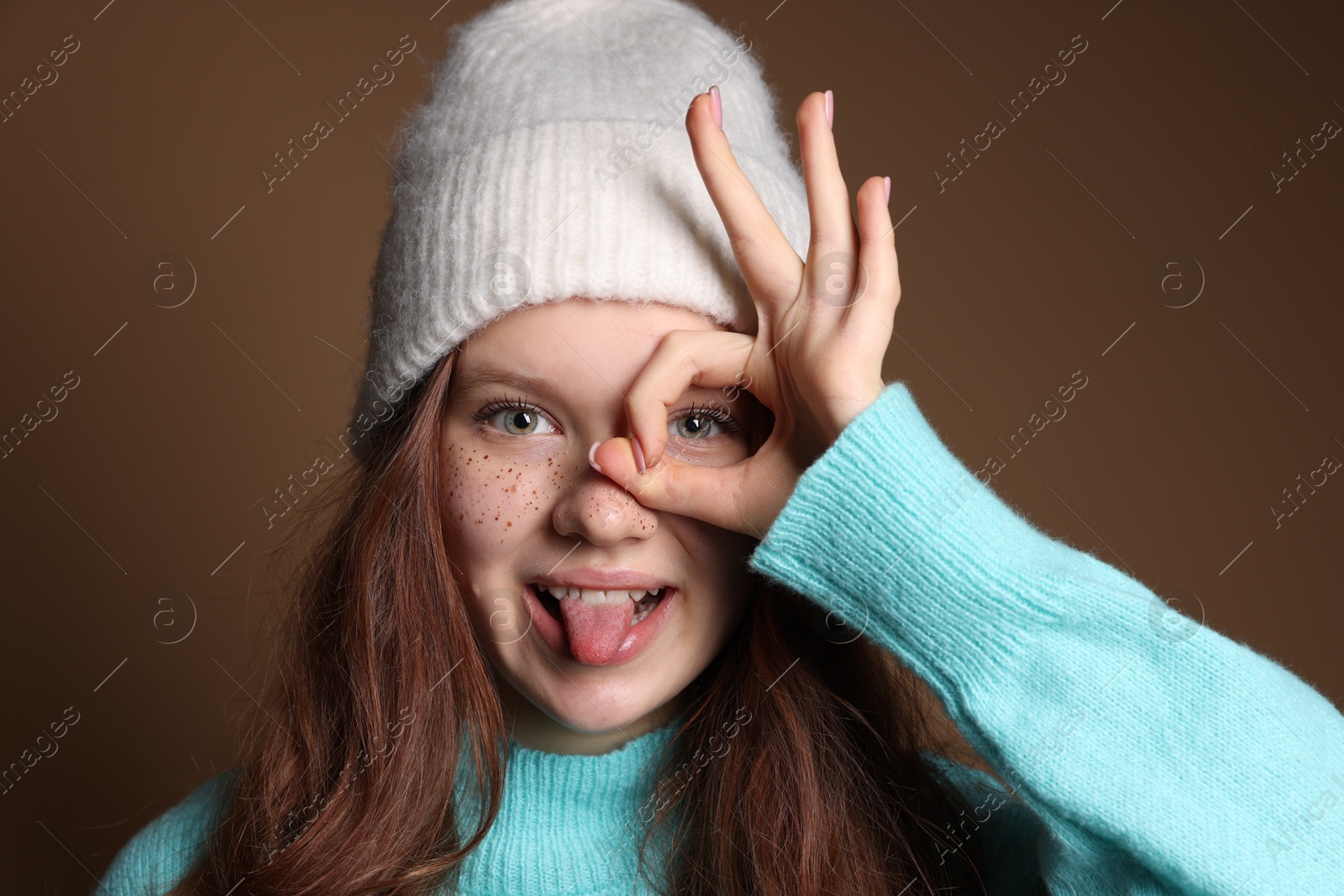 Photo of Cute teenage girl with freckles in hat on brown background, closeup