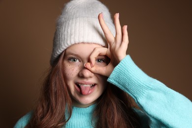 Photo of Cute teenage girl with freckles in hat on brown background, closeup