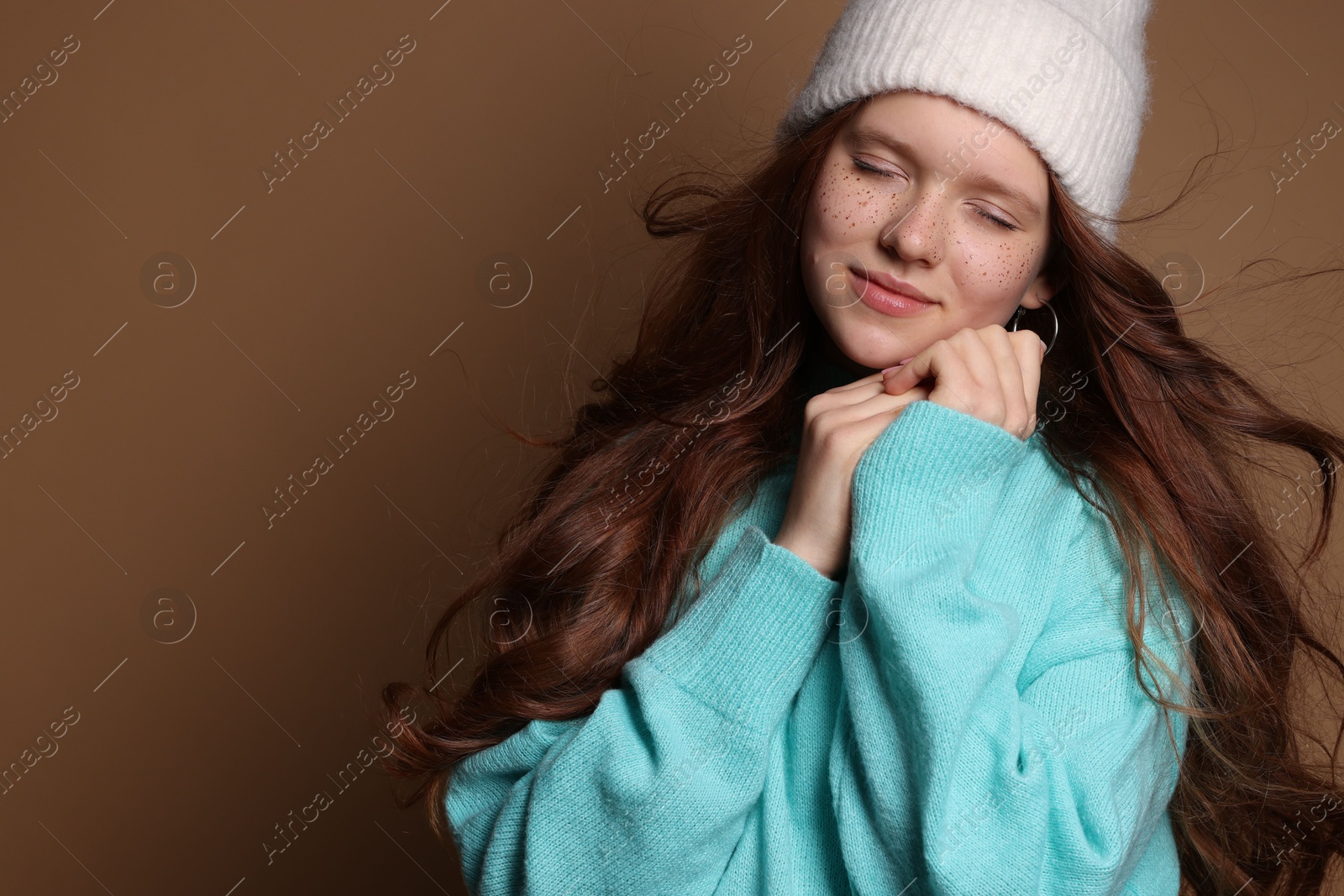 Photo of Beautiful teenage girl with freckles in hat on brown background, space for text