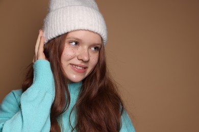 Photo of Beautiful teenage girl with freckles in hat on brown background, space for text