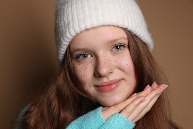 Photo of Beautiful teenage girl with freckles in hat on brown background, closeup