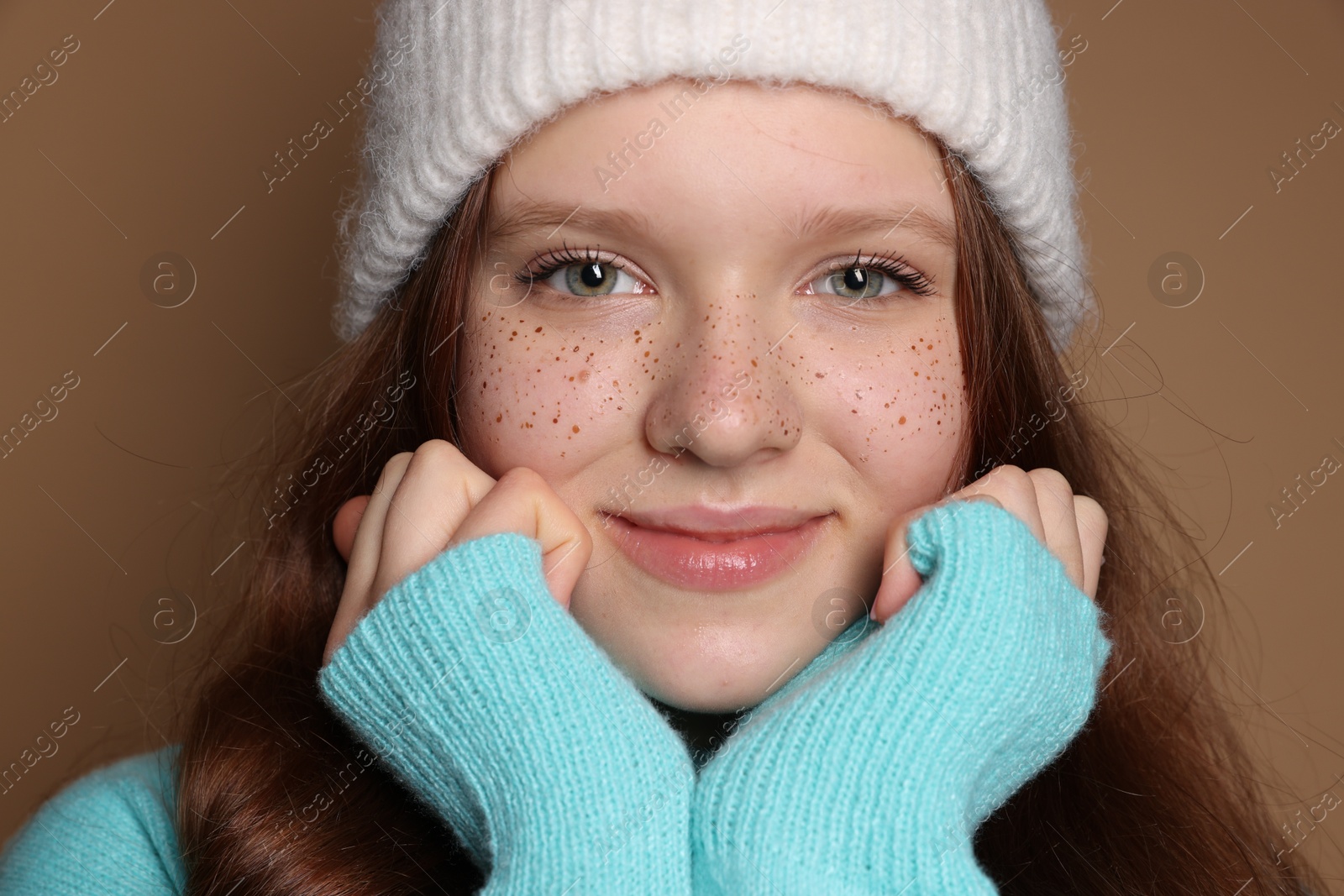 Photo of Beautiful teenage girl with freckles in hat on brown background, closeup