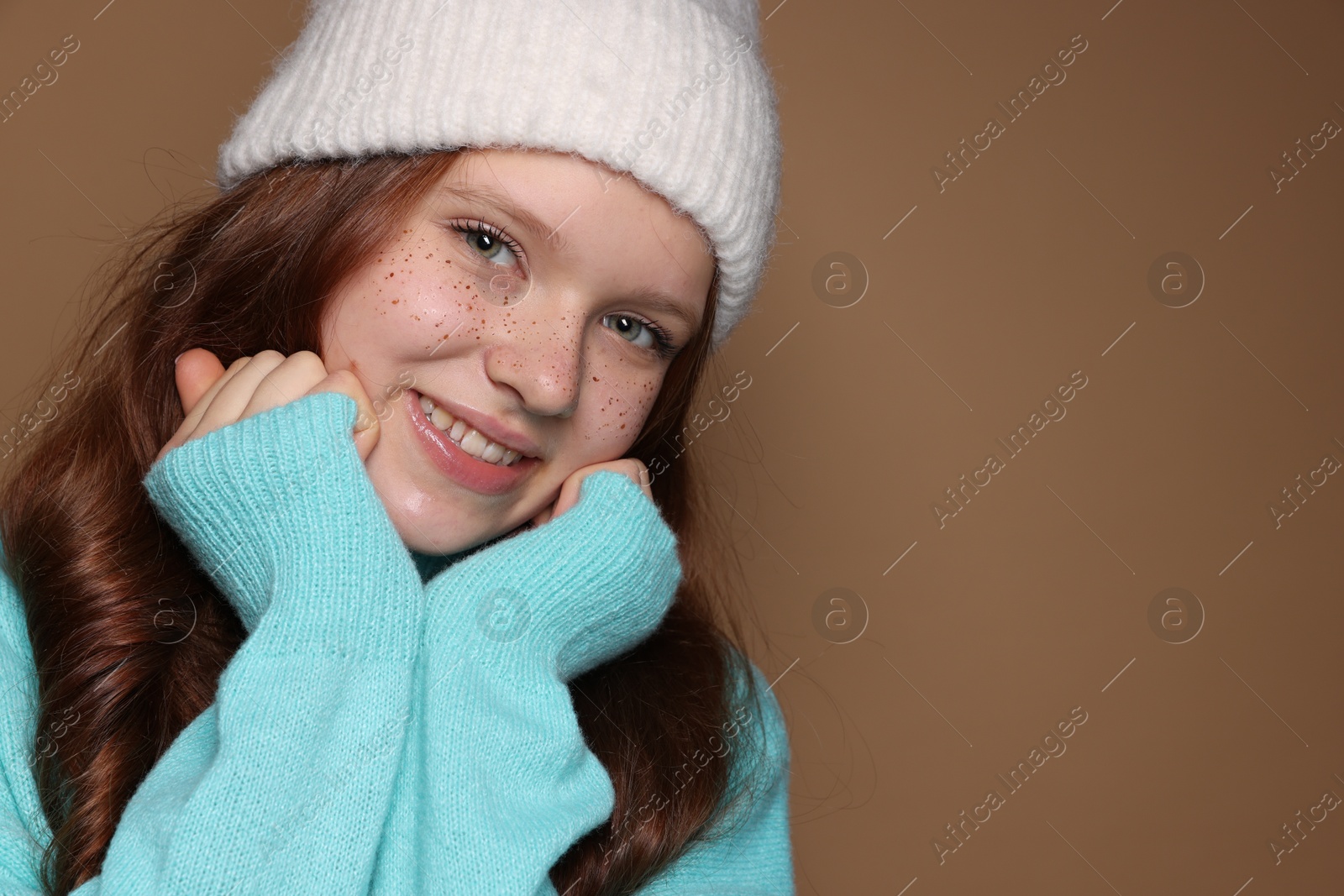 Photo of Beautiful teenage girl with freckles in hat on brown background, closeup. Space for text