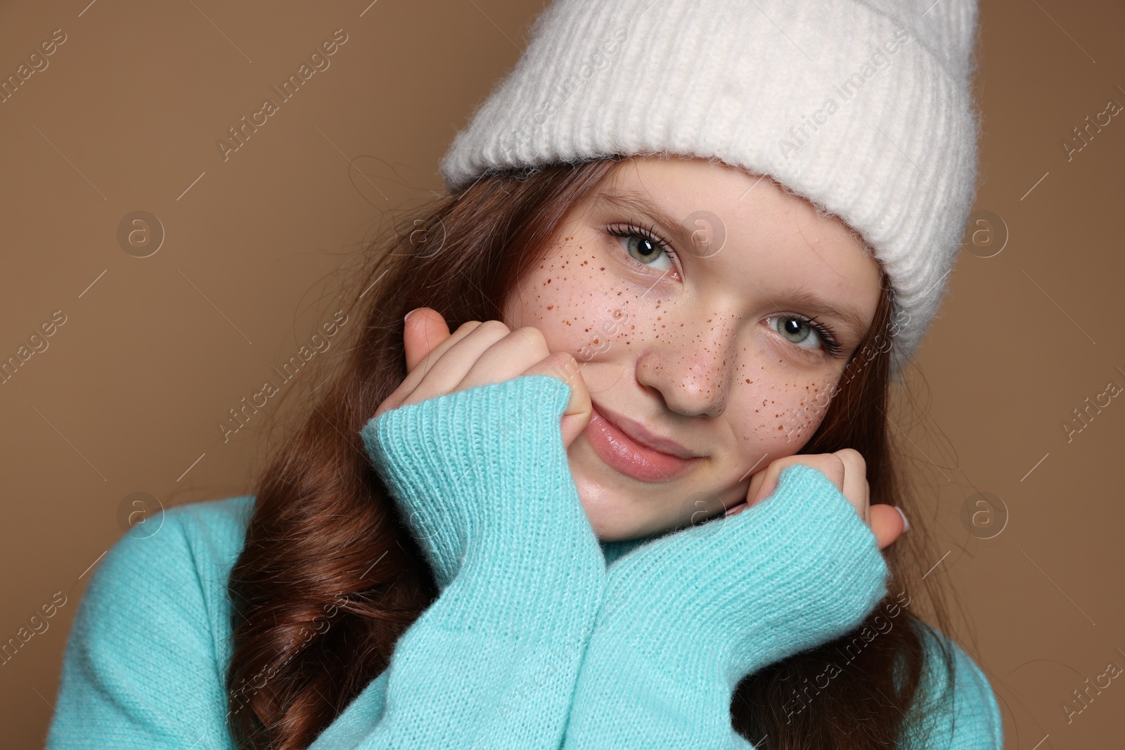 Photo of Beautiful teenage girl with freckles in hat on brown background, closeup