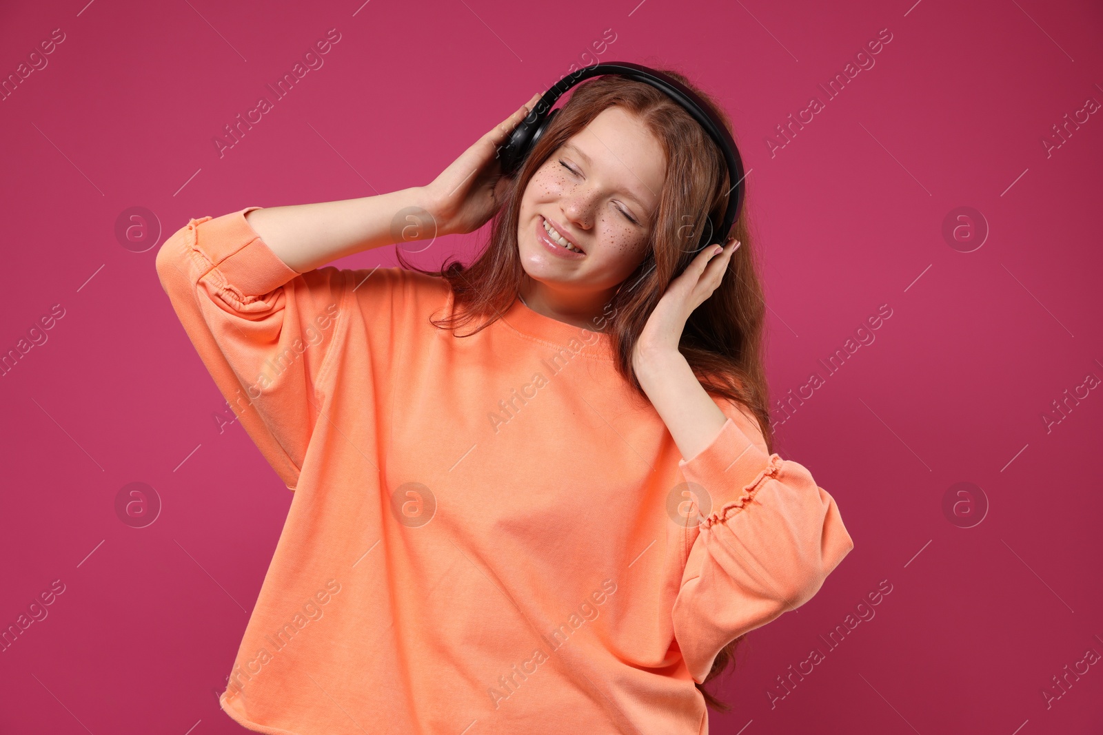 Photo of Beautiful freckled teenage girl with headphones on pink background