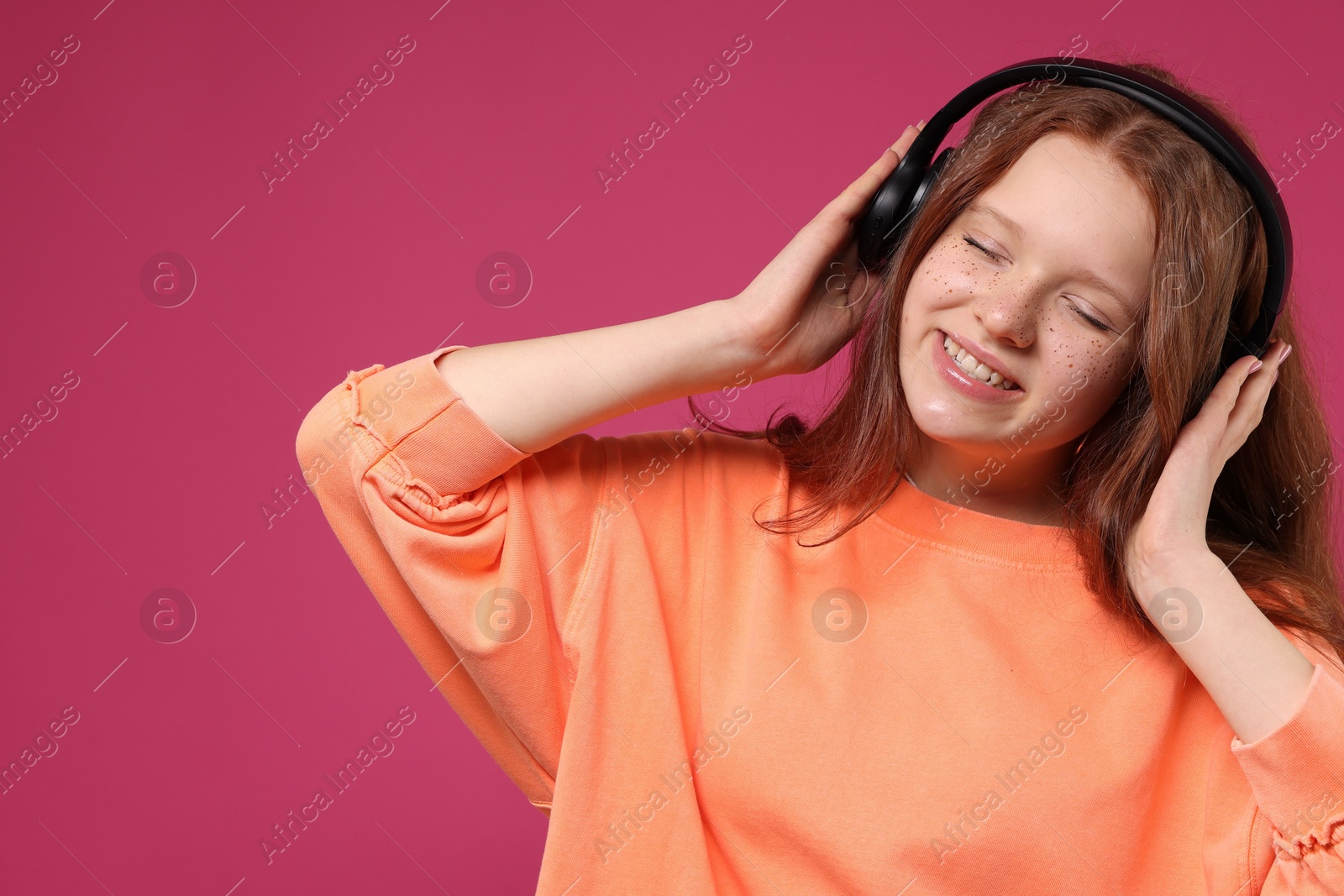 Photo of Beautiful freckled teenage girl with headphones on pink background