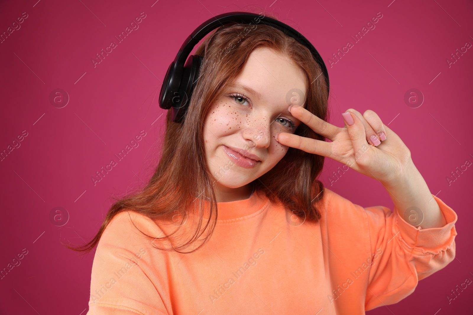 Photo of Beautiful freckled teenage girl with headphones taking selfie on pink background